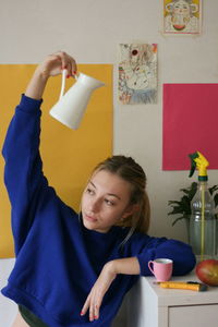 Young woman looking away while holding jug at home