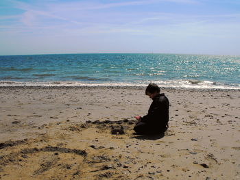 Man sitting on sea shore at beach against sky during sunny day