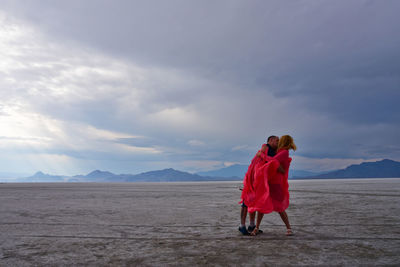 Full length of couple kissing while standing on ground against sky