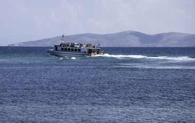 Ferry on sea by mountains against sky