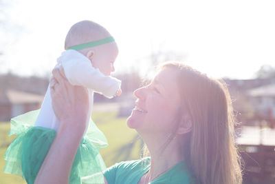 Smiling mother lifting baby girl against sky