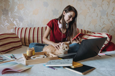 Young woman using mobile while sitting with cat on bed