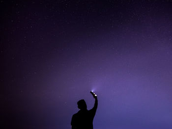Silhouette man holding illuminated flashlight against star field at night