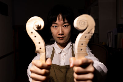 Young chinese woman violin maker showing the neck of the violins under construction in her workshop