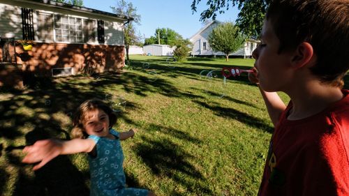 Side view of boy blowing bubbles while sister dancing at yard