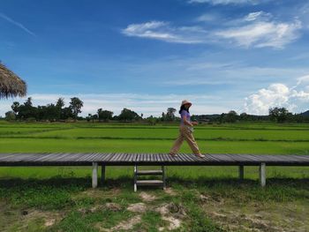 Man standing on bench in field against sky