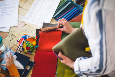 High angle view of fashion designer choosing textile from colorful swatch while baby girl playing with fabric picture bo