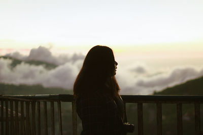 Woman standing by railing against sky during sunset