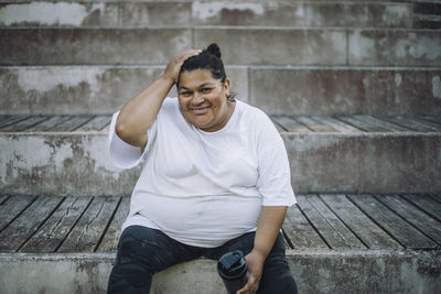 Portrait of smiling oversize woman with head in hand sitting on steps