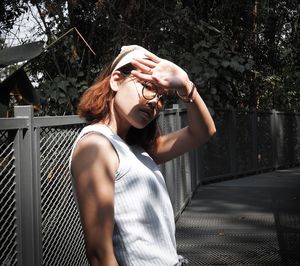 Portrait of young woman shielding eyes while standing on footpath