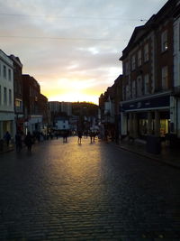 People walking on street amidst buildings in city at sunset