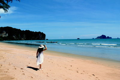 Rear view of woman walking on beach against sky