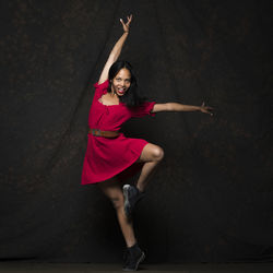 Full length of a young woman dancing against black background