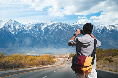 Rear view of man photographing on mountain road