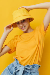 Portrait of young woman wearing hat standing against yellow background
