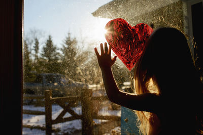 Girl drawing heart shape on window at home