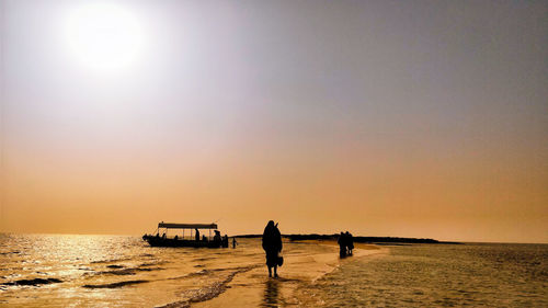 Silhouette people on beach against sky during sunset