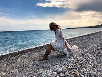 Young woman on rock at beach against sky