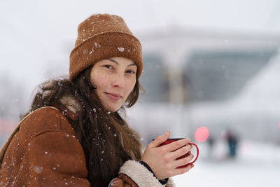 Young cute asian woman sitting on railway platform with mug of hot tea in snowy winter weather