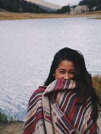 Portrait of woman wrapped in blanket against lake