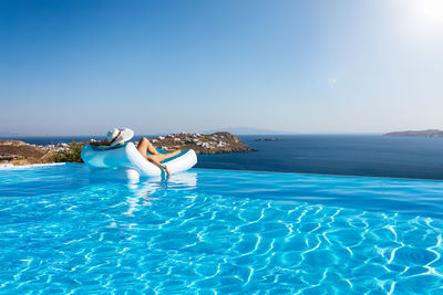 Rear view of woman relaxing against sea on lounge chair at infinity pool