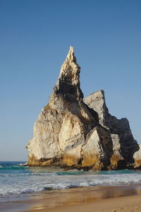 Rock formation on beach against clear blue sky