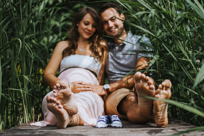 Husband and pregnant wife sitting with shoes amidst plants