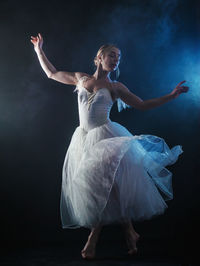 Ballet dancer wearing white dress dancing against black background