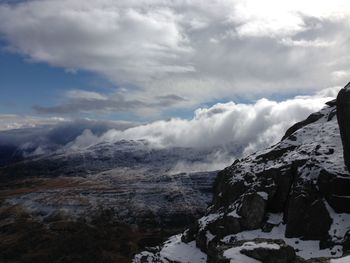 Scenic view of rocky mountains against cloudy sky on sunny day