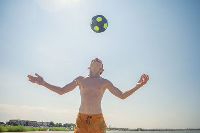 Rear view of shirtless man with arms raised against sky