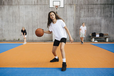 Pre-adolescent girl looking away while practicing basketball in court