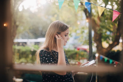 Young woman adjusting earphones while using mobile phone in balcony during party