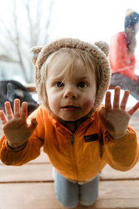 Young blonde kid pushes face and hands against glass during quarantine