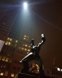 Low angle view of statue against illuminated buildings at night