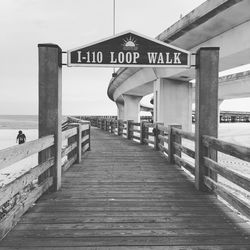 Low angle view of information sign on pier at beach against sky