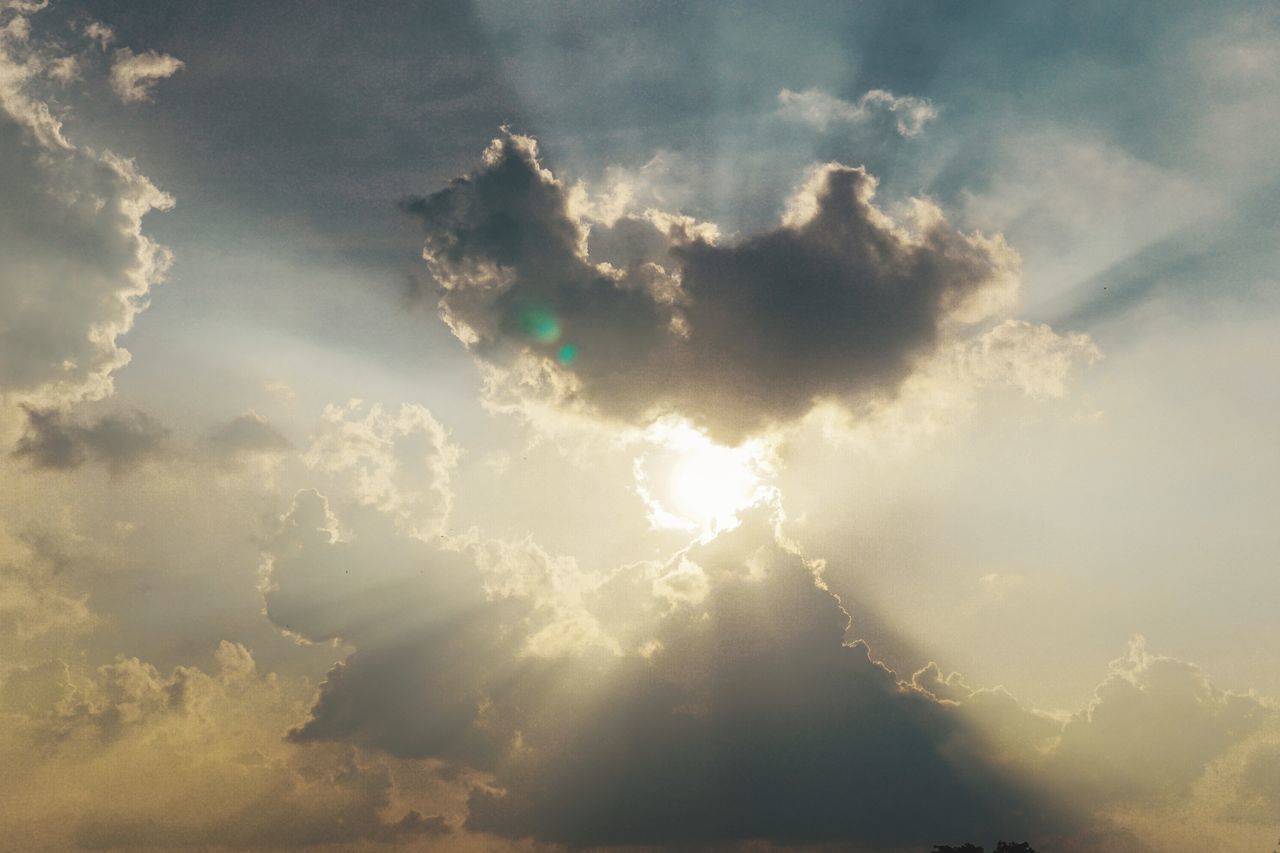 LOW ANGLE VIEW OF SUN STREAMING THROUGH CLOUDS IN SKY