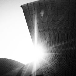 Low angle view of sunlight streaming through building against clear sky