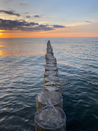 Wooden posts in sea against sky during sunset