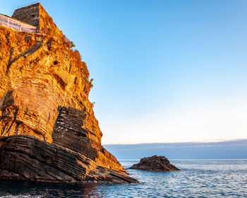 Rock formation in sea against clear blue sky