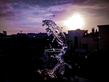 Illuminated fountain in city against sky during sunset