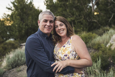 Portrait of happy couple embracing while standing against trees in forest