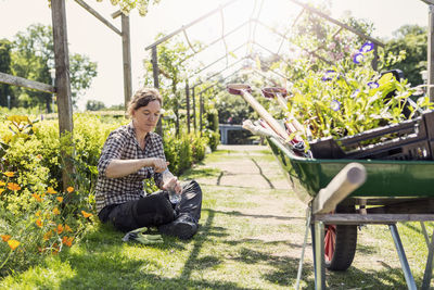 Woman opening water bottle while sitting in greenhouse