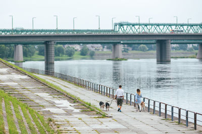 People with dogs walking on footpath by river against sky