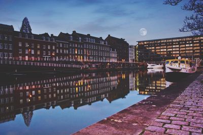 Buildings reflecting in canal against sky at dusk