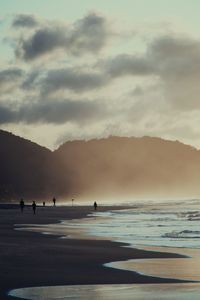 Silhouette people on beach against sky during sunset