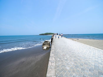 People on walkway at beach against blue sky