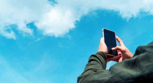 Low angle view of man using smart phone against sky