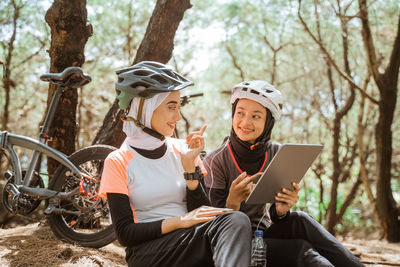 Smiling female friends using digital tablet sitting at park