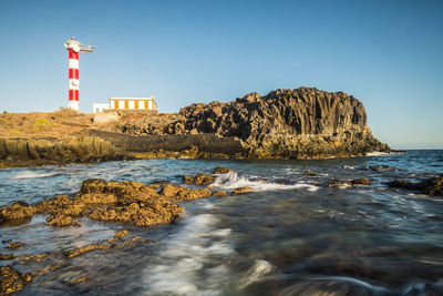 Lighthouse on beach by sea against sky