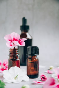 Front view of glass bottles of geranium essential oil with fresh pink and white flowers and petals